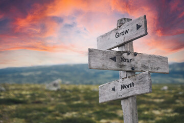 grow your worth text quote on wooden signpost outdoors in nature. Pink dramatic skies in the background.