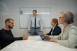 © Михаил Решетников - Caucasian man draws a graph on a white board, three colleagues sit at the table and listen to him.