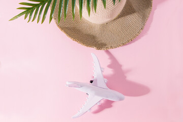 Summer composition with a beach hat, a tropical green palm leaf, and a white airplane on a pink pastel background. Minimal nature flat lay. Travel concept.
