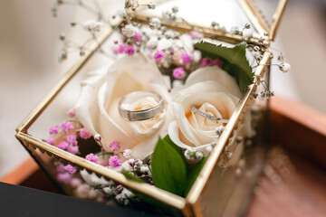 Wedding rings of the bride and groom in a glass box decorated with white roses. Wedding rings at the wedding ceremony. Beautiful bride and groom rings in white gold