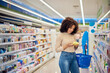 © bnenin - Black woman looking at some products for her hair, holding a basket, shopping alone.