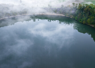 Wall Mural - Aerial view of fog above lake early in the morning during sunrise. Misty scenery with reflections.