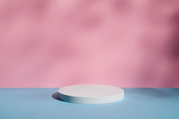 Empty white round podium and shadows on pink and blue background. Showcase for product presentation. Pedestal for beauty cosmetic advertising. Minimal still life in pastel colours. Copy space.