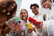© CarlosBarquero - Portrait of four smiling friends looking at cell phone from below. College classmates group happily gathered together using colorful mobile outside. Young people back to school and social networking.