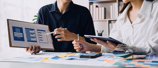 Close up ux developer and ui designer brainstorming about mobile app interface wireframe design on table with customer breif and color code at modern office.Creative digital development agency
