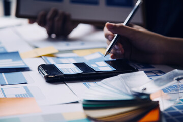 Close up ux developer and ui designer brainstorming about mobile app interface wireframe design on table with customer breif and color code at modern office.Creative digital development agency