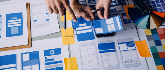 Close up ux developer and ui designer brainstorming about mobile app interface wireframe design on table with customer breif and color code at modern office.Creative digital development agency