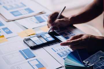 Close up ux developer and ui designer brainstorming about mobile app interface wireframe design on table with customer breif and color code at modern office.Creative digital development agency