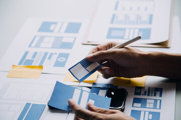 Close up ux developer and ui designer brainstorming about mobile app interface wireframe design on table with customer breif and color code at modern office.Creative digital development agency