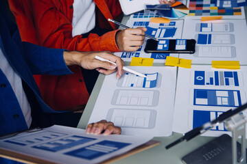 Close up ux developer and ui designer brainstorming about mobile app interface wireframe design on table with customer breif and color code at modern office.Creative digital development agency