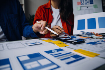 Close up ux developer and ui designer brainstorming about mobile app interface wireframe design on table with customer breif and color code at modern office.Creative digital development agency