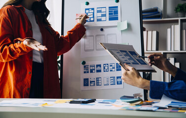 Close up ux developer and ui designer brainstorming about mobile app interface wireframe design on table with customer breif and color code at modern office.Creative digital development agency