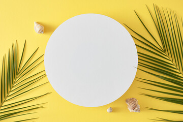 Wall Mural - Summer fun concept. Top view flat lay of palm leaves and seashells on light yellow background with blank circle for text or advert