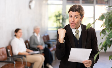 Wall Mural - Adult man in business suit posing with documents in his hands in office space