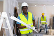 © JackF - African-american repairman wearing protective hardhat and yellow vest carrying construction detail while working in building site in apartment.