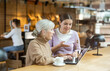 © JackF - Positive old and young women drinking and enjoying coffee while using laptop in cafe
