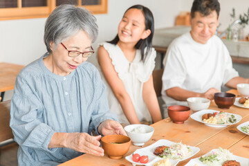 家のダイニングで家族団欒して食事する子供と夫婦・親子・三世代家族（二世帯住宅）
