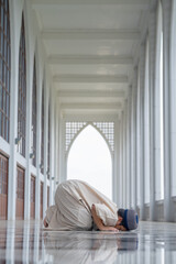 Wall Mural - A little Asian Muslim boy is praying with peace in the beautiful mosque in the evening, giving a powerful atmosphere of faith, with copy space, islam concept.