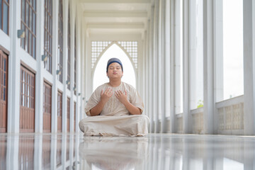 Wall Mural - A little Asian Muslim boy is praying with peace in the beautiful mosque in the evening, giving a powerful atmosphere of faith, with copy space, islam concept.