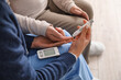 Young caregiver measuring sugar level of senior woman at home, closeup