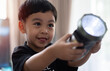 © Kunlathida - Asian toddler in black costume shines a flashlight forward in the room and smiles with joy at what he sees.