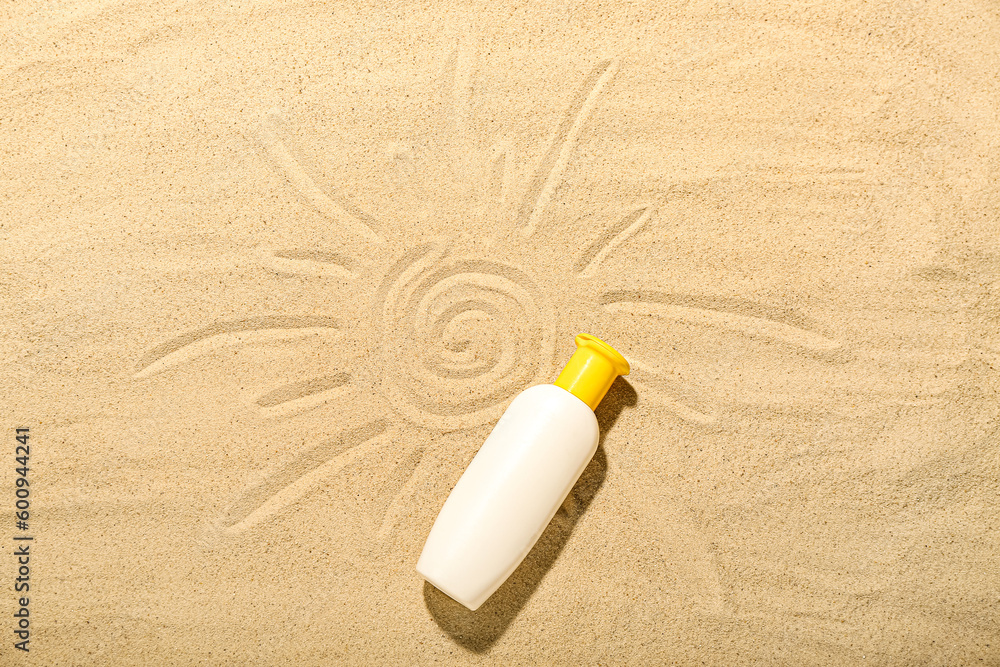 Creative composition with bottle of sunscreen cream with drawings on sand