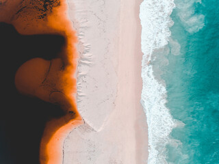 Wall Mural - Aerial view of where the river meets the sea. Vibrant orange and dark river meet turquoise sea waves on beach in Western Australian town called Guilderton.
