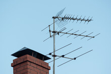 TV Antenna On Red Roof. Television Antenna On Roof With Blue Sky. Brick Pipe House And Media Transmitter, Radio