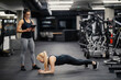 © Dusan Petkovic - A happy female fitness instructor is holding tablet and looking at the sportswoman who is doing planks in a gym.