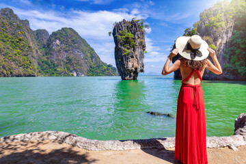 Wall Mural - A tourist woman in a red dress looks at the famous sightseeing spot James Bond island at Phang Nga Bay, Phuket, Thailand