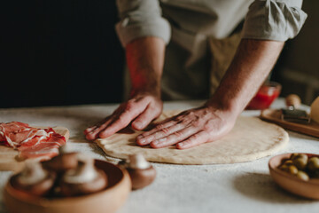 Wall Mural - Man preparing pizza on a white table against black background