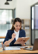 © crizzystudio - Beautiful attractive Asian businesswoman holding a clipboard of documents sitting analytically analyzing various marketing management information the finances were at her desk in the office at ease.