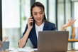 © crizzystudio - Attractive Asian businesswoman doing business related to village building project contacting using a mobile phone to chat and Negotiate management ideas in her office.