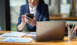 © crizzystudio - Attractive Asian businesswoman doing business related to village building project contacting using a mobile phone to chat and Negotiate management ideas in her office.