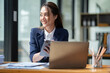 © crizzystudio - Asian businesswoman in a suit sitting holding iPad or tablet in contact See details and discuss business information happily in the office.