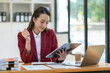 © crizzystudio - Beautiful attractive Asian businesswoman holding a clipboard of documents sitting analytically analyzing various marketing management information the finances were at her desk in the office at ease.