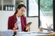 © crizzystudio - Confident Asian businesswomen sitting at their desks Are using banking applications to buy or pay online mobile bills. and registered her credit card on the website for online purchases.