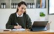 © crizzystudio - Confident Asian businesswoman happily sitting and taking notes online with a laptop computer in the office.