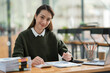 © crizzystudio - Young Asian businesswoman holding a pen sitting and analyzing the details of management information Finance is happy at the desk in the office.