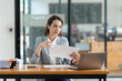© crizzystudio - Asian businesswoman sitting happily in office holding detailed report paper analyzing data accuracy in financial matters management concept.