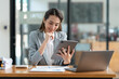 © crizzystudio - Asian businesswoman in a suit sitting holding iPad or tablet in contact See details and discuss business information happily in the office.