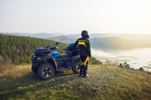  Man With Helmet Standing Near Quad Bike In The Mountains And Enjoying Beautiful View Of Nature At Sunset.