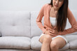 © Prot - Sick Asian Woman Suffering From Acute Abdominal Pain in the abdomen due to menstruation period, PMS.  Sitting On Couch, stomachache from food poisoning, abdominal pain, digestive problem, gastritis