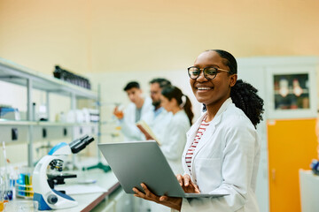 Wall Mural - happy black biochemist working on laptop in lab and looking at camera.