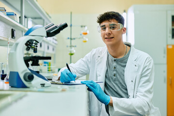 Wall Mural - happy biochemistry student taking notes during lab research and looking at camera.