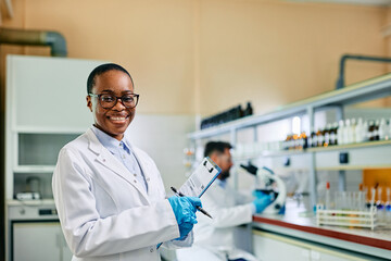 Happy black female biotechnologist working in lab and looking at camera.