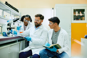 Wall Mural - happy chemist and his younger colleagues analyzing liquid in beaker in laboratory.