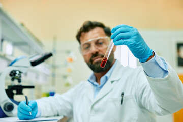 Wall Mural - Close up of biochemist working with red liquid sample in laboratory.