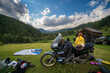Setting up a blue tent with a great view of the mountains. A trip on a motorbike. A touring motorcycle with lots of gear. Bags, luggage. A couple of bikers, stopped for the night in a camp.
