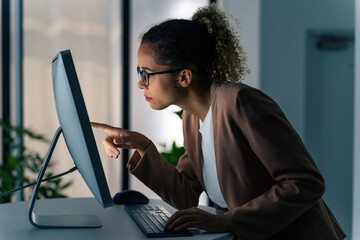 Black woman using desktop PC in dark office.